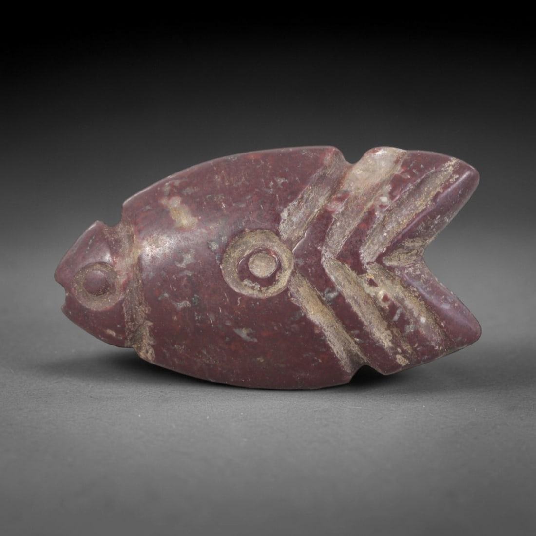 Ancient Stone Fish - Near Eastern Amulet Figurine, 62AP: This artifact is carved from deep red stone with a weathered, earthy patina and subtle mineral inclusions, exhibiting stylized piscine features consistent with ancient Near Eastern stoneworking techni