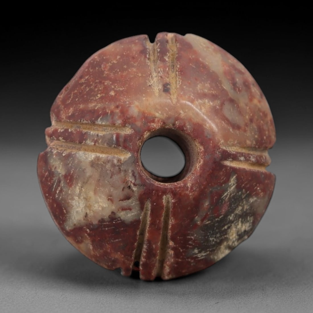 Ancient Stone Sun Amulet - Near Eastern Carved Pendant, 3AG: This amulet is carved from a mottled red and beige stone with a weathered, earthy patina and natural mineral inclusions. The form is a circular disk with a central drilled hole, and four sets of paire
