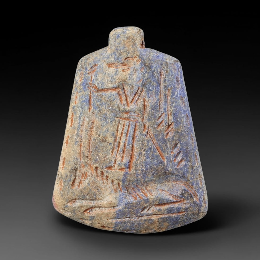 Ancient Lapis Lazuli Amulet - Near Eastern Hunter Figurine, 16BA: Carved from lapis lazuli, the amulet takes a bell-shaped form with a suspension loop at the top, designed for wear as a protective talisman. The front face is incised with a stylized standing hunter f