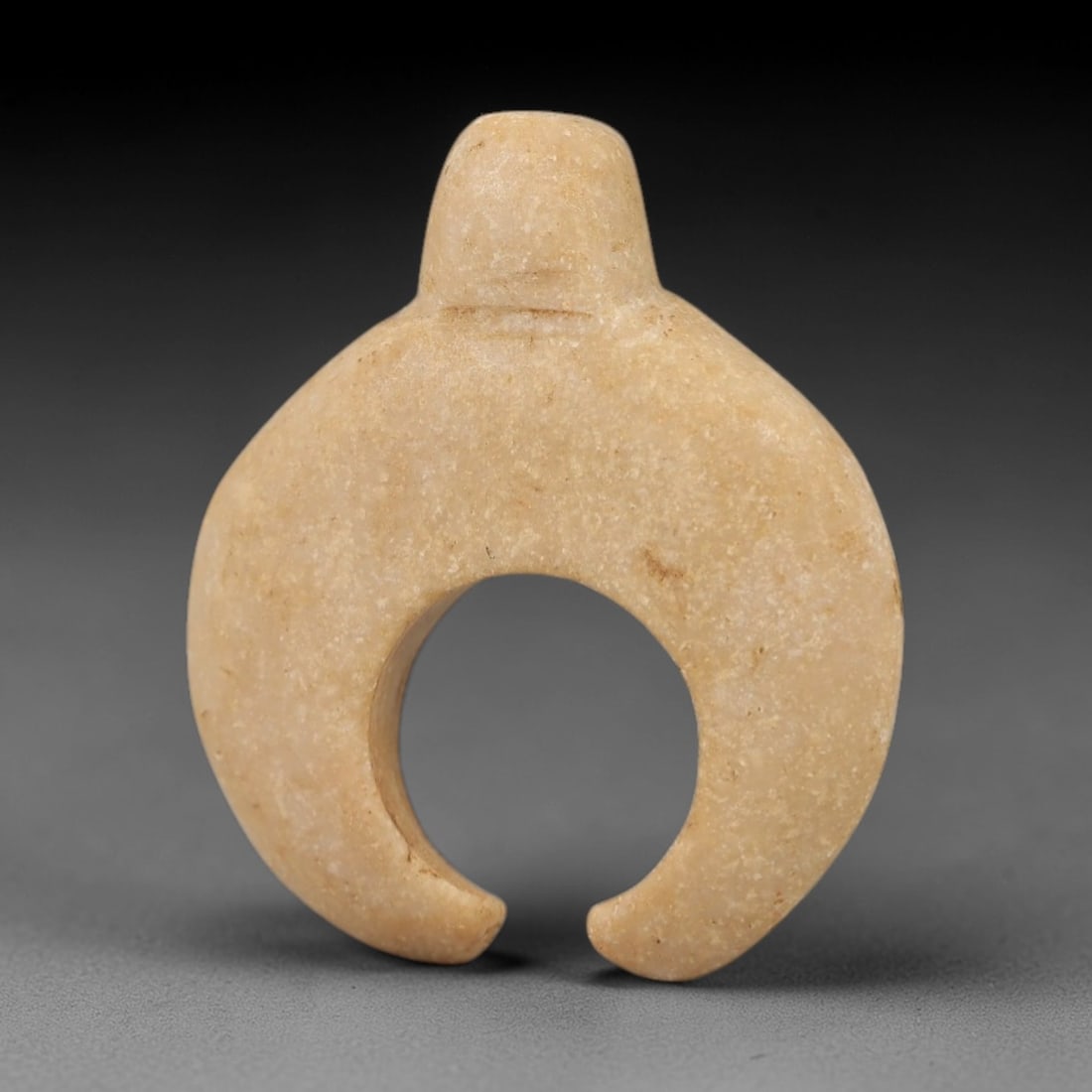 Ancient Beige Stone Amulet - Egyptian Style Figurine, 2AG: Carved from beige stone, this ancient Egyptian-style amulet features a compact, crescent form with a suspension hole at the top, indicating its use as a wearable amulet. The carving exhibits primitive