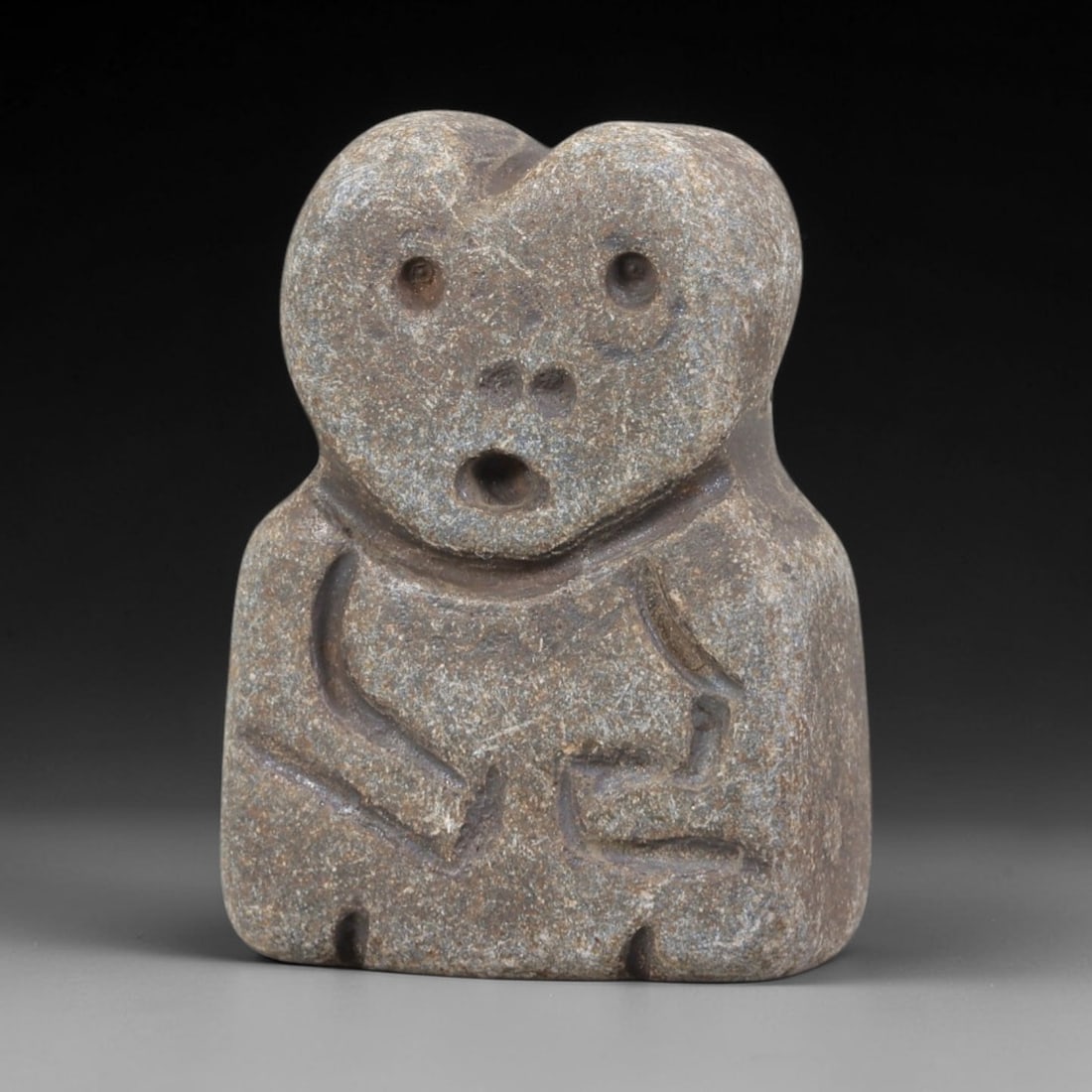 Ancient Stone Idol - Near Eastern Figurine, 18FY: Carved from a compact rectangular stone, this idol features a stylized head with a heart-shaped upper contour, circular eye perforations, paired nasal holes, and an open mouth, paired with a torso inc
