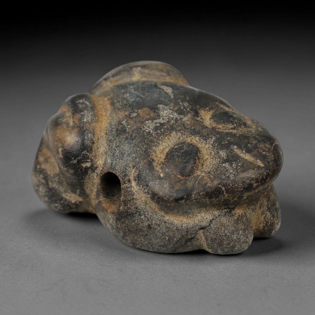 Ancient Stone Frog Amulet - Near Eastern Relic, 1AE: Carved from dark stone with earthy mineral encrustations, this amulet takes the form of a squatting frog, a motif associated with water and fertility symbolism in ancient Near Eastern iconography. The