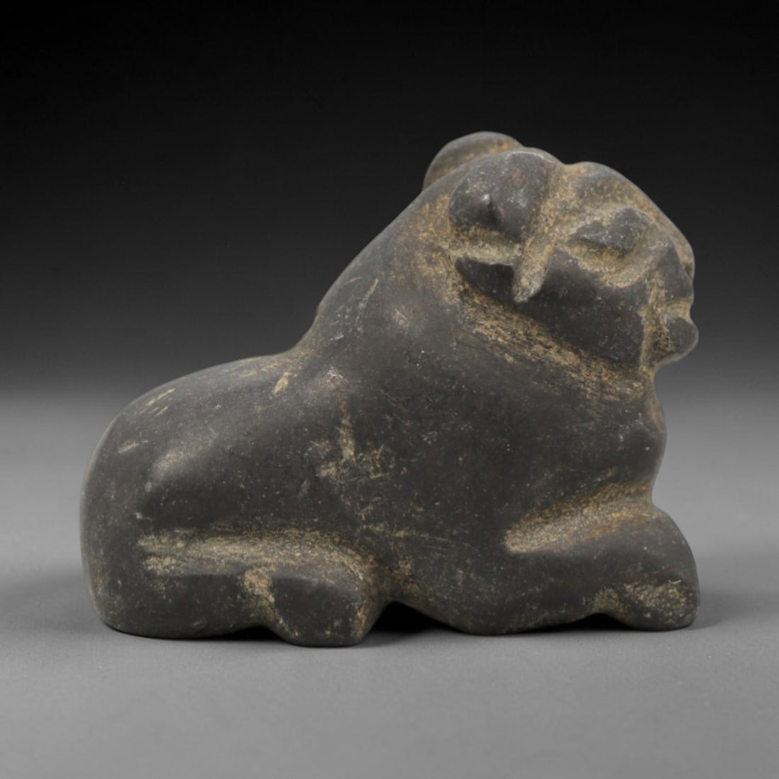 Ancient Near Eastern Stone Ram Amulet - Carved Figurine, 96ZW: This amulet is carved from a dense, dark grey stone, likely basalt or a similar igneous rock, with incised linear details defining its recumbent ram form. The piece depicts a ram in a resting pose, wi