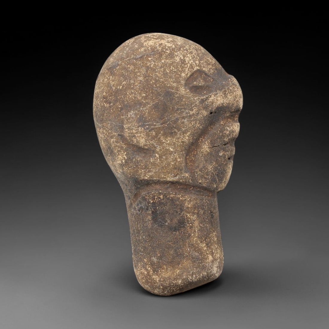 Ancient Stone Maskette - Near Eastern Amulet Figurine, 41WJ: Carved from stone, this ancient Near Eastern amulet takes the form of a maskette, featuring a simplified yet distinct facial structure with incised carvings defining the facial features and neck. The