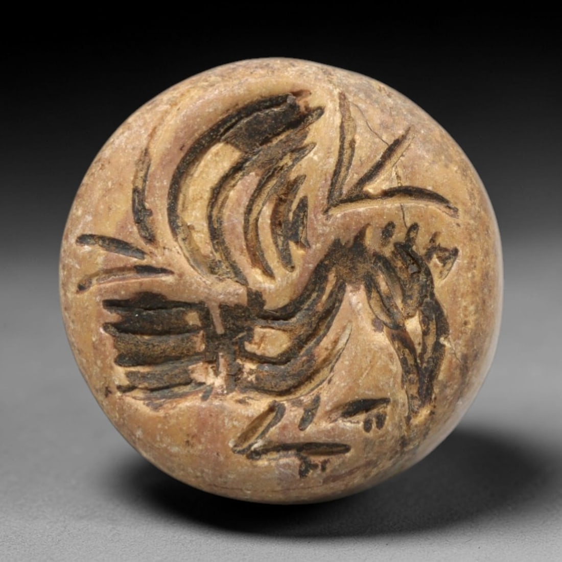 Ancient Near Eastern Stone Bird Amulet - Stamp Seal, 61ZR: This artifact is a carved stone stamp seal amulet, crafted from a granular, tan-brown stone with a matte surface and dark pigment filling the incised details. The circular seal face depicts a stylized