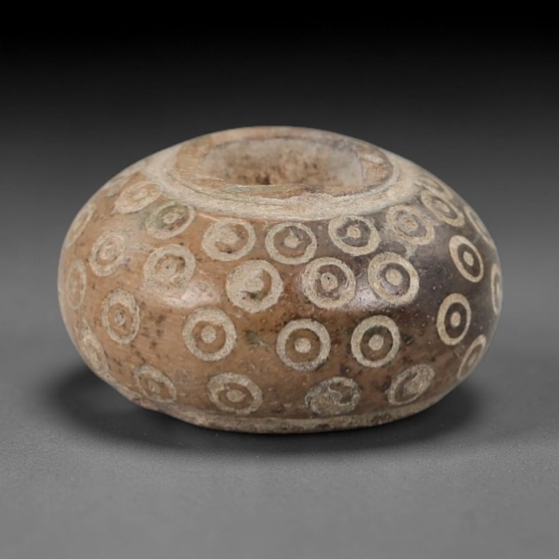 Ancient Near Eastern Bone Spindle Whorl - Dot-in-Circle Motif, 86AH: Carved from ancient bone, this Near Eastern spindle whorl features a continuous dot-in-circle motif encircling its central perforation, a design with apotropaic significance in ancient Near Eastern cu