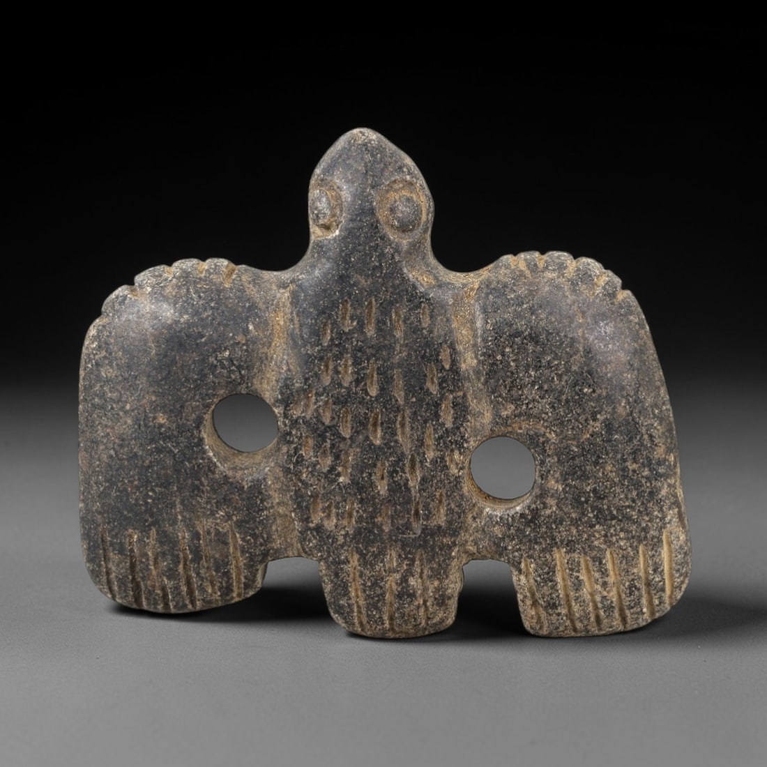 Ancient Stone Vulture Amulet - Near Eastern Bird Figure, 27AM: This vulture amulet is carved from dark speckled stone, depicting a stylized bird of prey (vulture) with outstretched wings and a compact body. The piece features incised linear and stippled detailing
