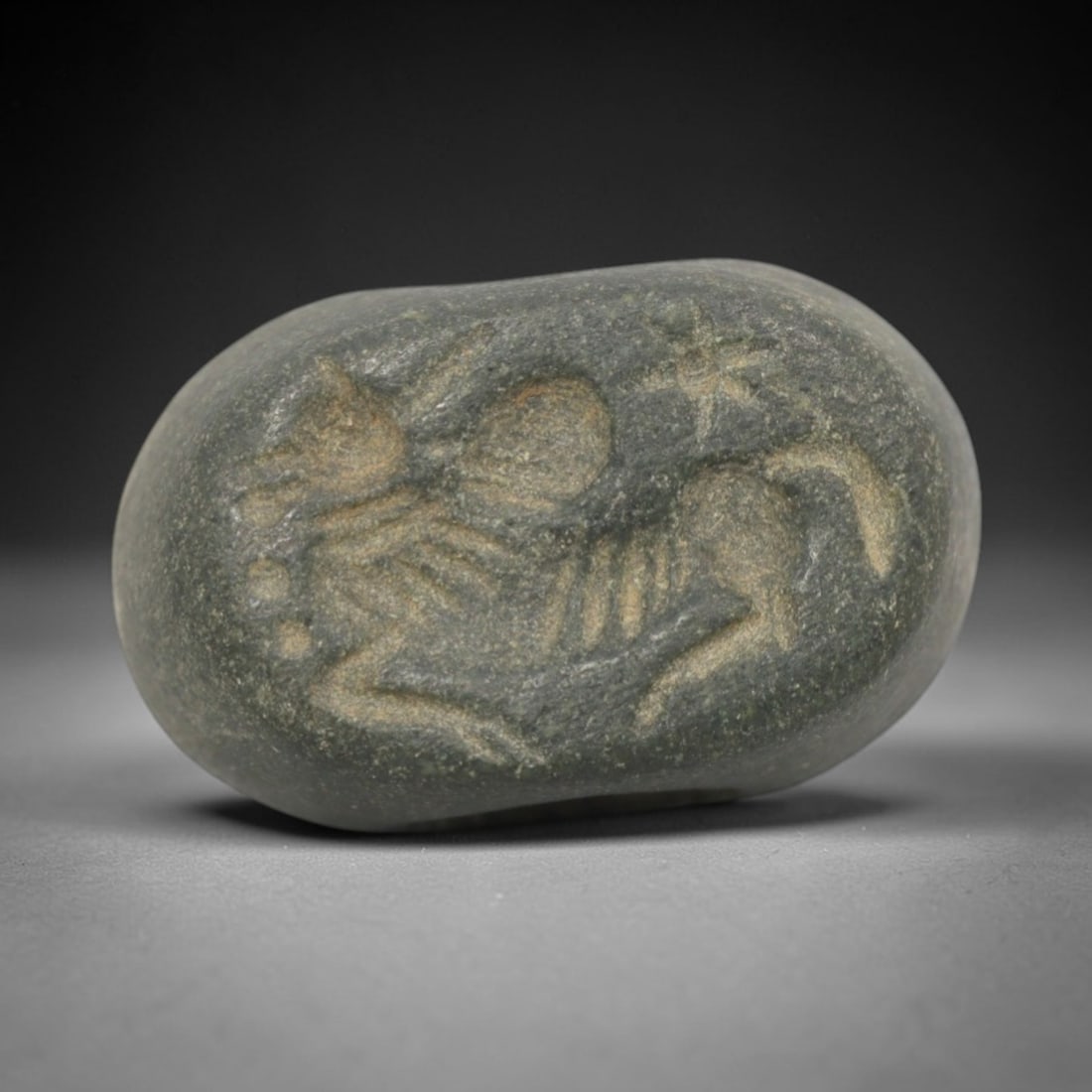 Ancient Stone Hemispherical Stamp Seal - Near Eastern Mythical Creature Figure, 100ZS: Crafted from dense, dark green stone, this hemispherical stamp seal bears incised carving of a mythical hybrid creature, likely a winged equine or sphinx, with a stylized head, radiating appendages, a