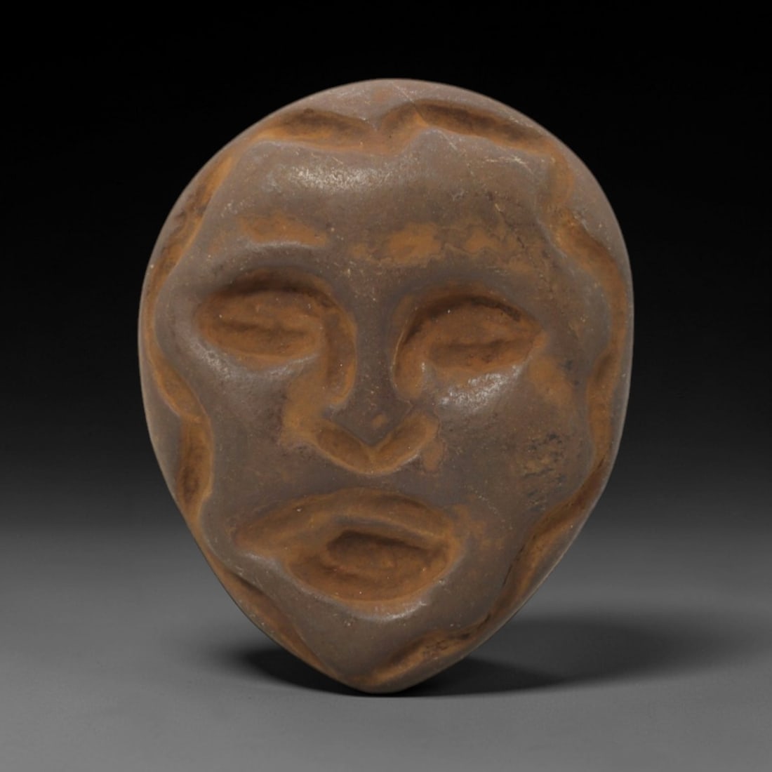 Ancient Stone Maskette - Anthropomorphic Ritual Figurine, 81FW: Carved from a smooth, earthy stone, this maskette presents a stylized human face within a rounded, teardrop-shaped form, featuring recessed eye sockets, a defined nasal ridge, and a hollowed mouth. Th
