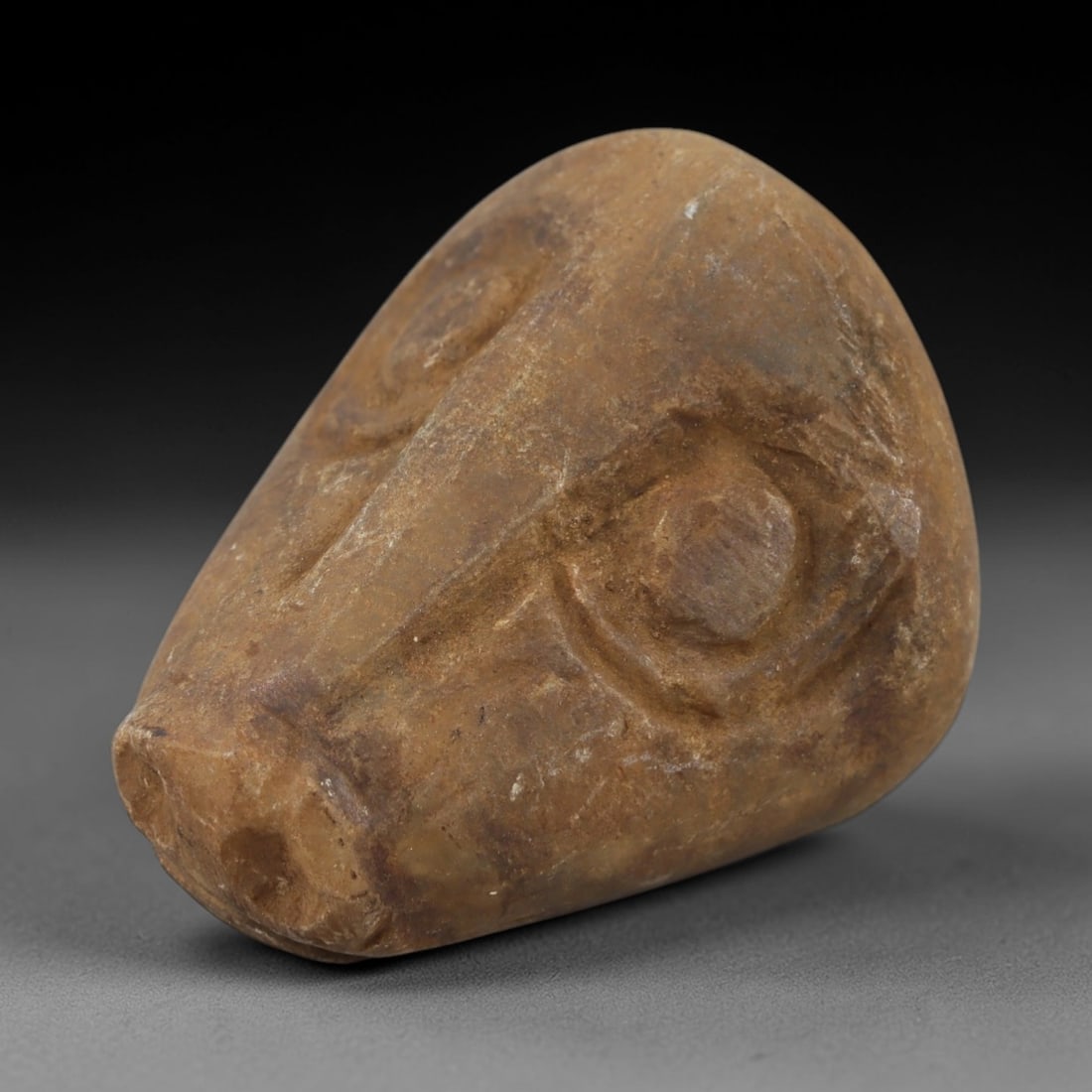 Ancient Steatite Ram Head Bead - Achaemenid Amulet, 27AH: Carved from steatite, this ancient Achaemenid ram head bead features a stylized, naturalistic rendering of a ram's head with detailed facial features and a central perforation for suspension. The ston