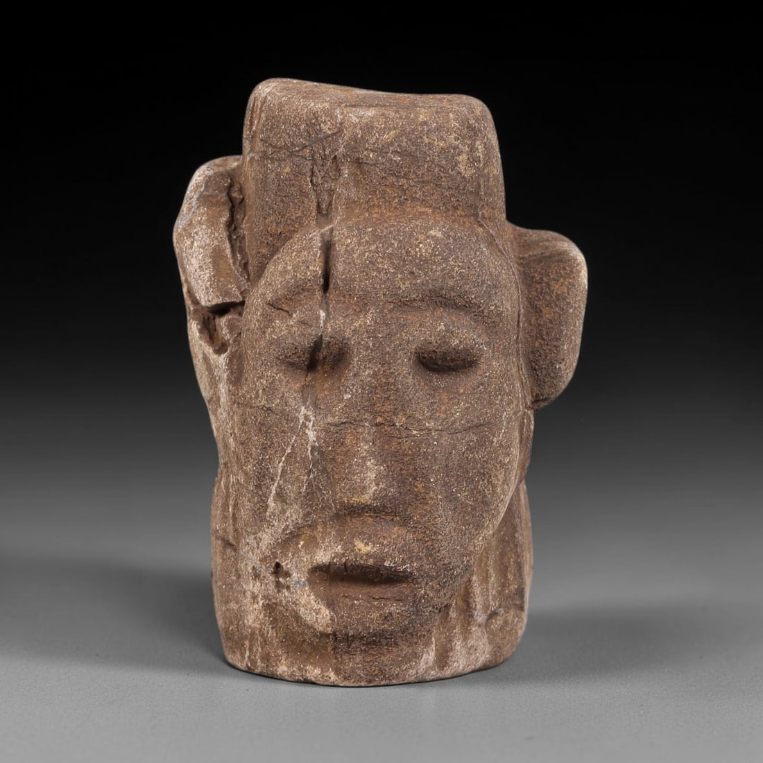Ancient Stone Maskette - Near Eastern Anthropomorphic Head, 57WJ: Carved from a coarse, porous stone, this artifact takes the form of a stylized anthropomorphic maskette or head fragment, rendered with simplified, archaic facial features. The eyes are carved as rece