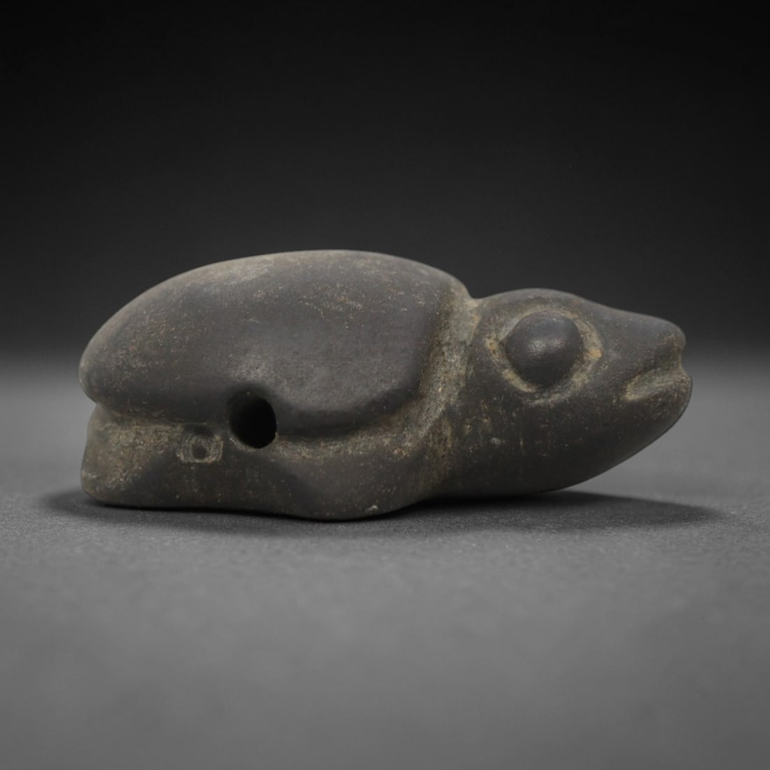 Ancient Near Eastern Dark Stone Turtle Amulet - Carved Pendant Figure, 2ZV: This amulet is carved from a dense, dark grey stone, likely siltstone or steatite, with subtle sculpted details defining its stylized recumbent turtle form. The piece features a smooth, domed carapace