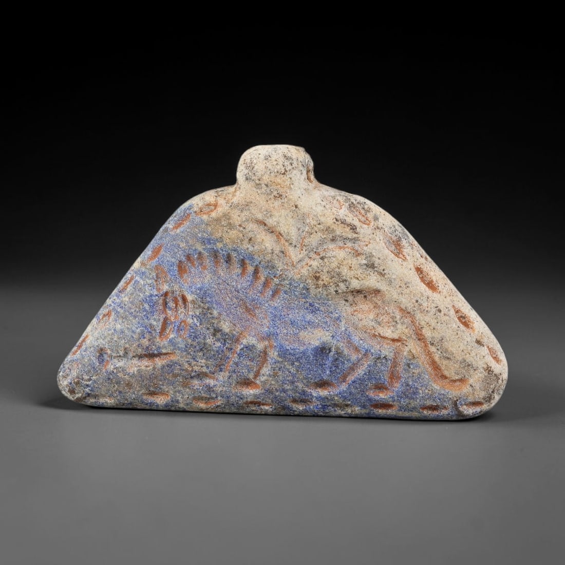 Ancient Lapis Lazuli Amulet - Near Eastern Animal Figurine, 2BA: Carved from lapis lazuli, the amulet takes a triangular, roof-shaped form with a suspension loop at the top, designed for wear as a protective talisman. The front face is incised with a stylized quadr