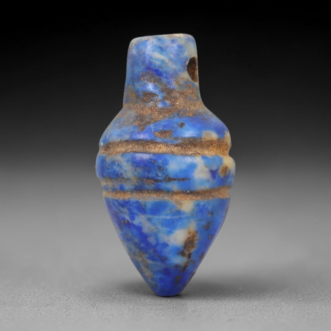 Ancient Lapis Lazuli Amulet - Egyptian Teardrop Pendant, 8AP: Carved from lapis lazuli, this amulet features a tapering, teardrop-like form with a narrow upper lug pierced for suspension, its body marked by three incised horizontal bands that define its segmente