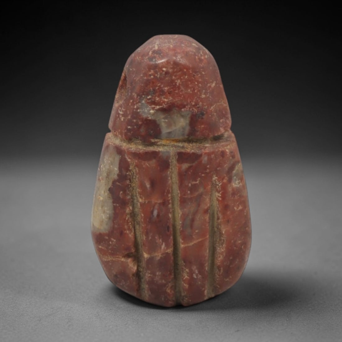 Ancient Stone Scarab Amulet - Egyptian Pendant, 71XQ: Carved from a rich reddish stone with lighter inclusions, this amulet takes the iconic form of the Egyptian scarab beetle, featuring a domed head, segmented body, and incised vertical linear details r