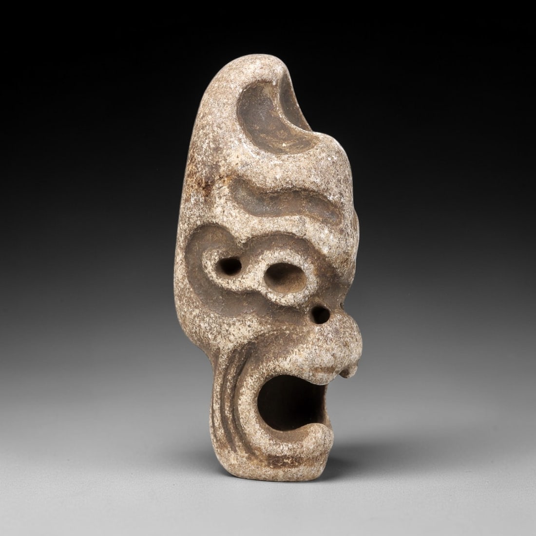 Ancient Stone Anthropomorphic Maskette Amulet - Near Eastern Figurine, 91FX: Carved from a weathered granular stone, this anthropomorphic amulet depicts a stylized, expressive face with deep relief carvings defining the eye sockets, nasal perforation, and a wide open mouth. Th