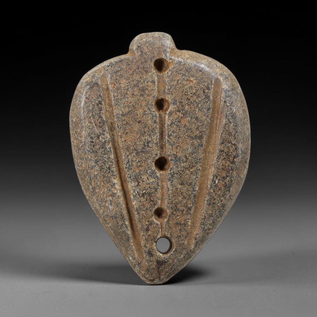 Ancient Schist Leaf-Shaped Amulet - Near Eastern Carved Pendant, 37BA: Carved from schist, the amulet takes the form of a stylized leaf or shield-shaped pendant with a drilled suspension lug at the top for wear. The surface features a central vertical channel with four d