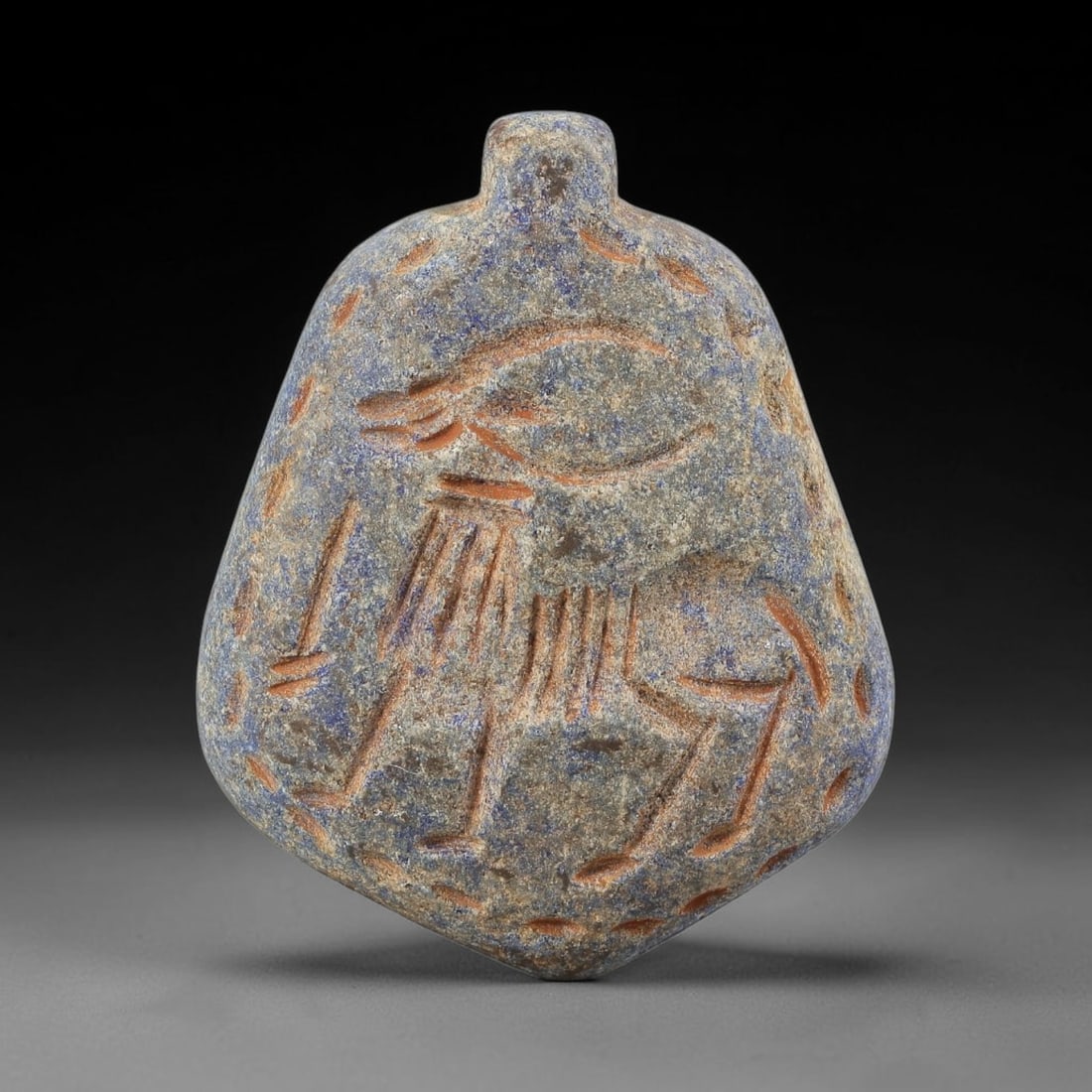 Ancient Lapis Lazuli Amulet - Near Eastern Animal Figurine, 21BA: Carved from lapis lazuli, the amulet takes a rounded, shield-shaped form with a suspension loop at the top, designed for wear as a protective talisman. The front face is incised with a stylized quadru