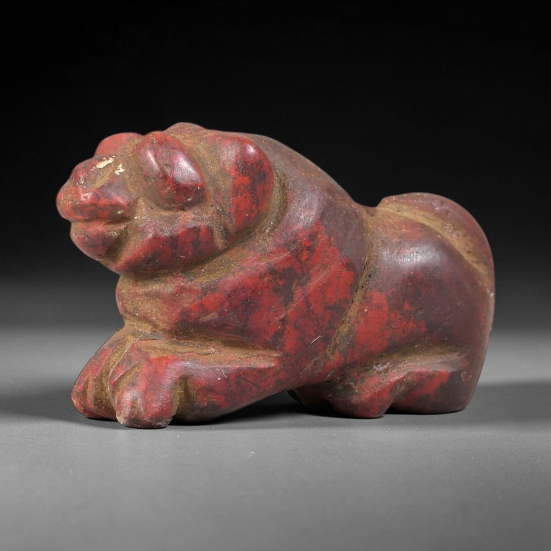 Ancient Red Stone Lion - Egyptian Amulet Figurine, 25AS: This amulet is carved from dense red stone, exhibiting a rich, earthy patina indicative of long-term burial. The form depicts a recumbent lion, rendered in a stylized, compact manner characteristic of
