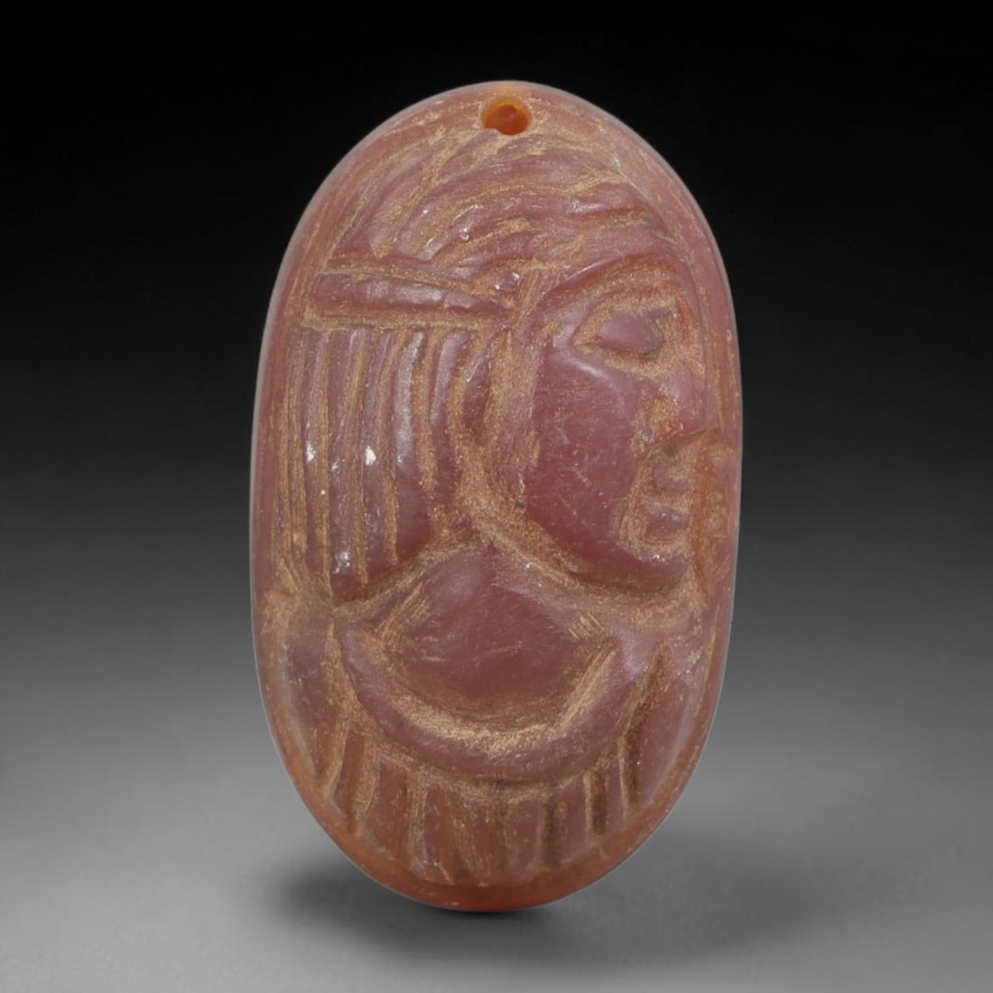 Ancient Carnelian Amulet - Near Eastern Bust Pendant, 58FY: Carved from carnelian, the amulet is an oval disc with a drilled suspension hole at the top, crafted in the ancient Near Eastern style. The front surface bears a raised relief portrait of a human bust