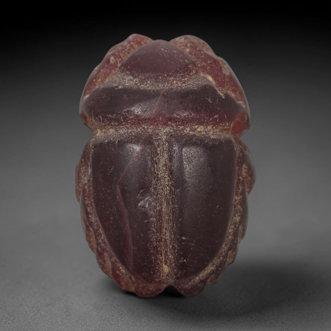 Ancient Red Jasper Scarab Amulet - Egyptian Figurine, 75AJ: Carved from deep, saturated red jasper, this amulet is formed as a stylized scarab beetle with incised linear detailing to define segmented head plates, central body ridge, and wing case contours, con