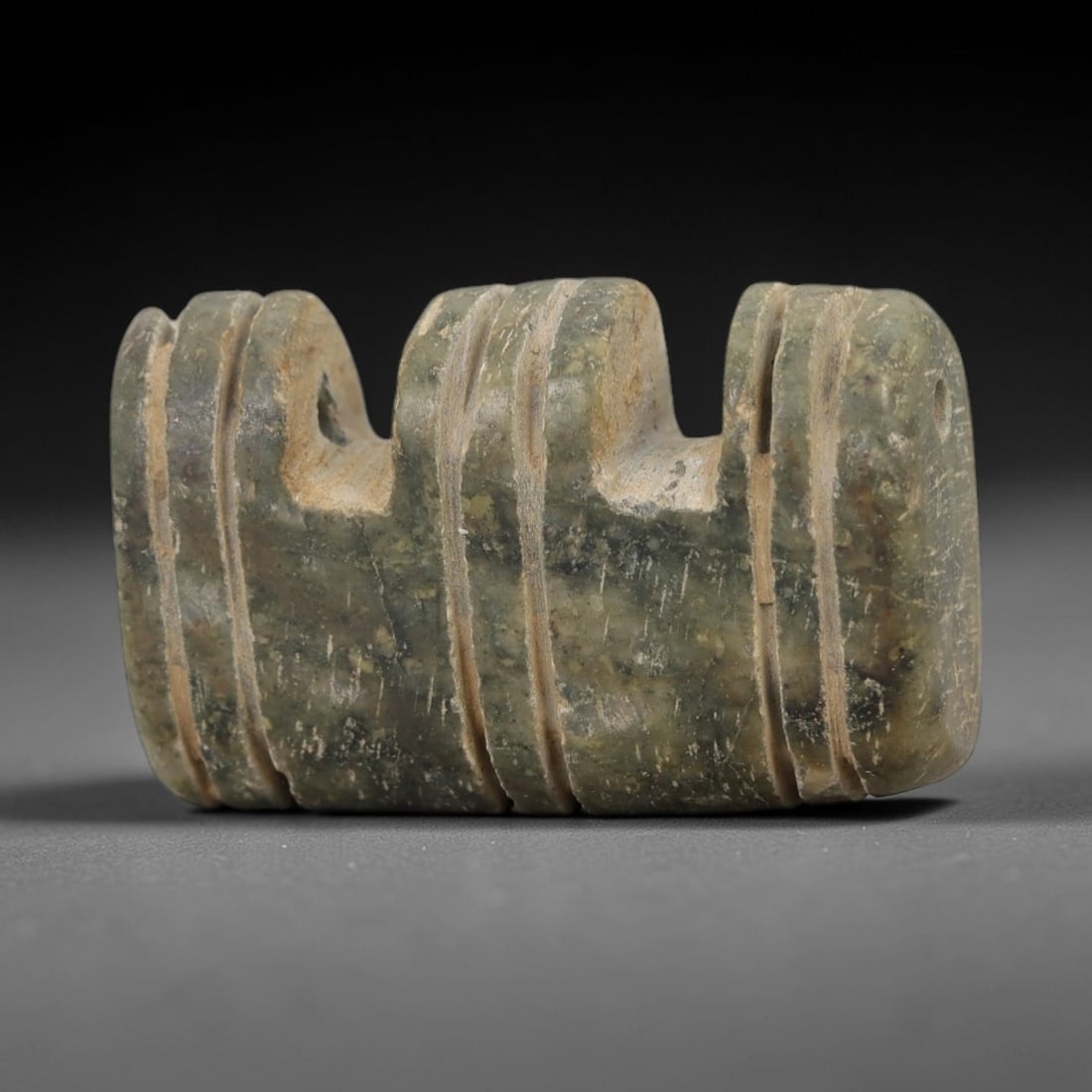 Ancient Stone Double Loop Amulet - Near Eastern Pendant, 45AG: This amulet is carved from a mottled greenish-gray stone with a weathered, earthy patina and visible mineral inclusions. The form is a rectangular block with three vertical sets of parallel incised gr