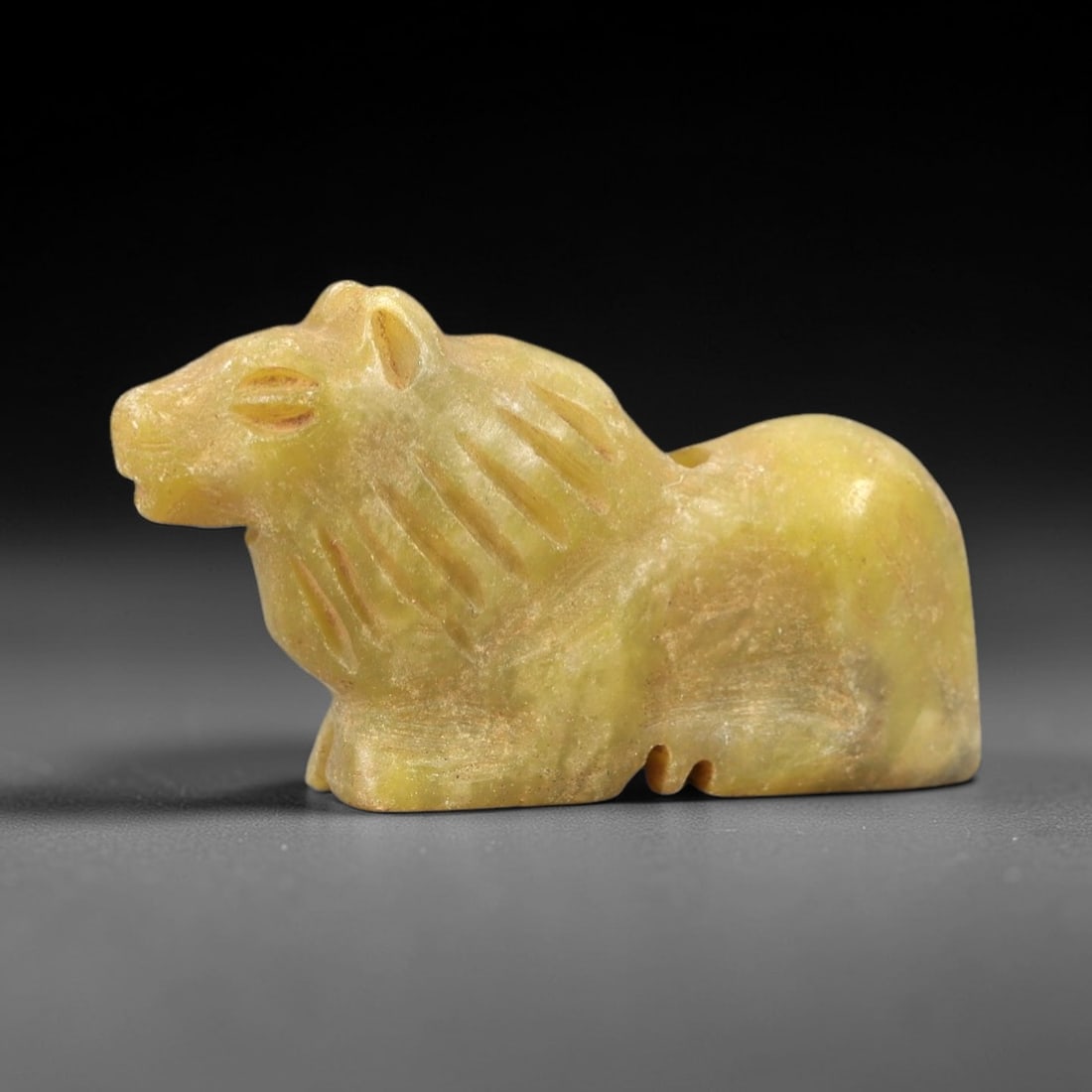 Ancient Serpentine Bovid Figurine - Near Eastern Amulet, 32AK: Carved from pale yellow-green serpentine, this reclining bovid figurine features stylized pointed ears, incised slit eyes, and linear detailing defining its mane. The compact, rounded body incorporate