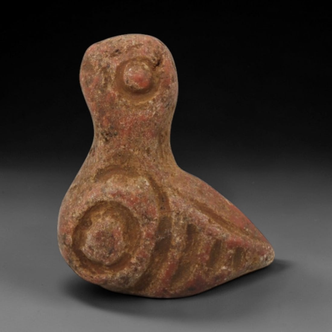 Ancient Stone Bird - Near Eastern Amulet Figurine, 20XR: Carved from warm reddish-brown stone, this amulet depicts a stylized seated bird with incised circular and linear details representing facial features and feather patterns. The geometric, abstract for