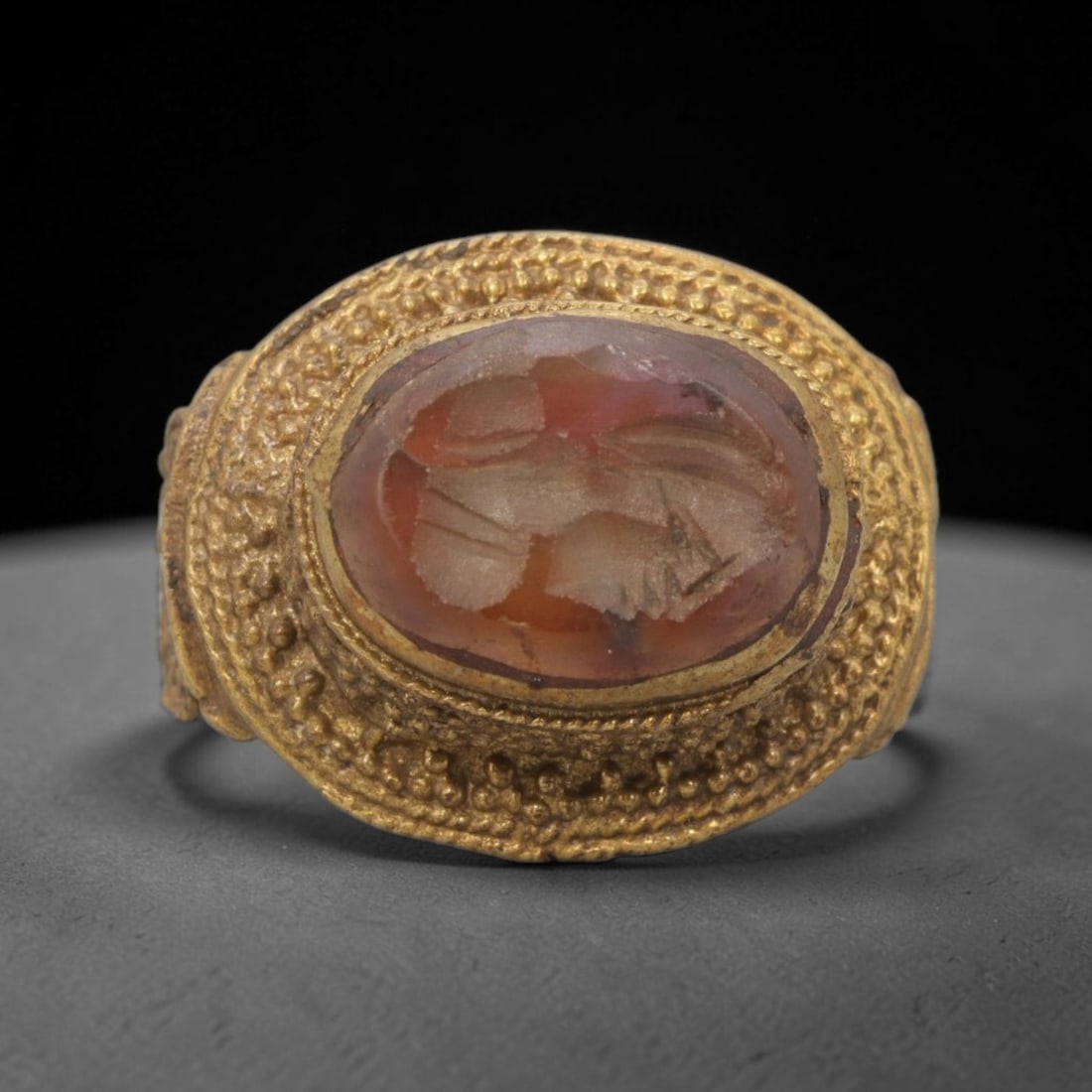Antique Qajar Dynasty Brass Carnelian Intaglio Ring - Size 9 US, 66ZX: This antique Qajar dynasty brass intaglio ring features an oval carnelian intaglio inset with incised figural carvings, set within an ornate brass mount adorned with granular beading detailing. The ri