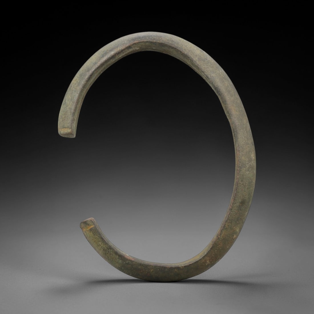 A Roman Bronze Bracelet, 1st-3rd Century CE, 25FV: Cast from bronze with a thick, flattened rectangular section, the bracelet is formed as an open C-shape with squared, slightly tapered terminals. The surface is covered in a uniform dark greenish-brow