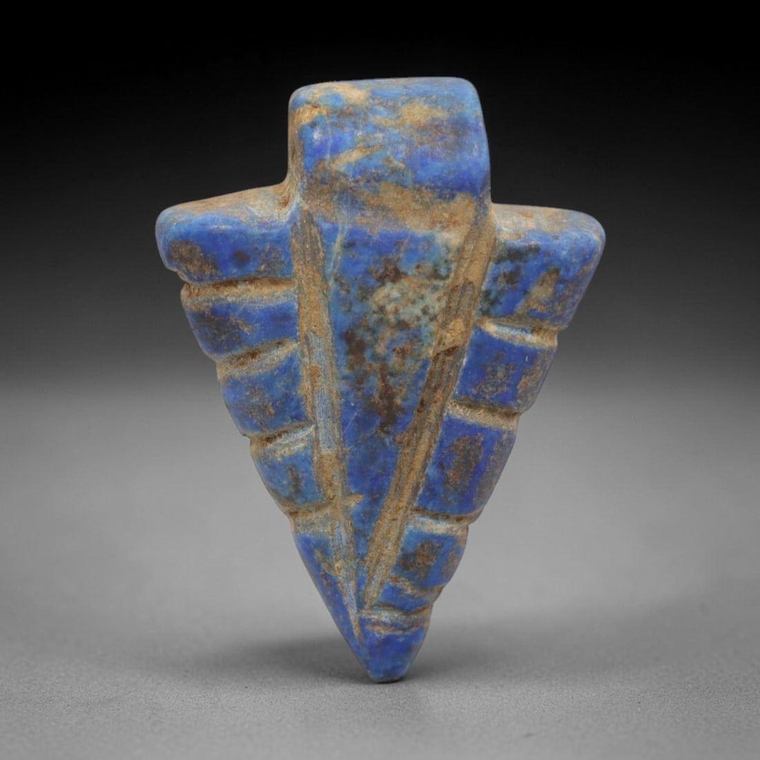 Ancient Lapis Lazuli Amulet - Egyptian Arrowhead Pendant, 29ZT: Carved from lapis lazuli, this amulet is formed in the shape of an arrowhead, with a rectangular upper lug pierced for suspension, its surface incised with vertical and horizontal lines that define th