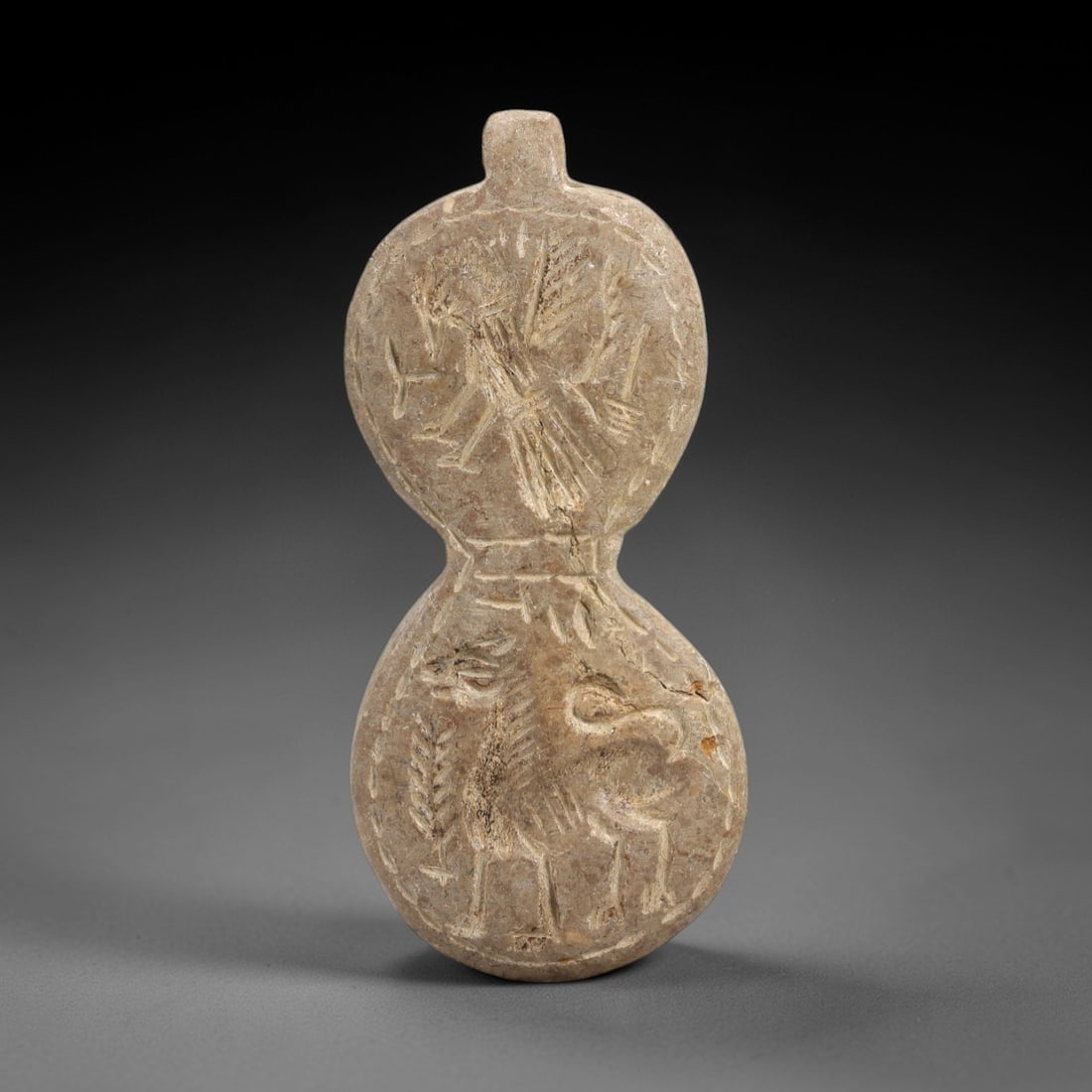 Ancient Stone Amulet - Near Eastern Bird Figure, 6AM: This double-lobed amulet is carved from soft stone, exhibiting the characteristic incised relief technique of ancient Near Eastern glyptic art. The upper lobe depicts a winged avian figure in dynamic