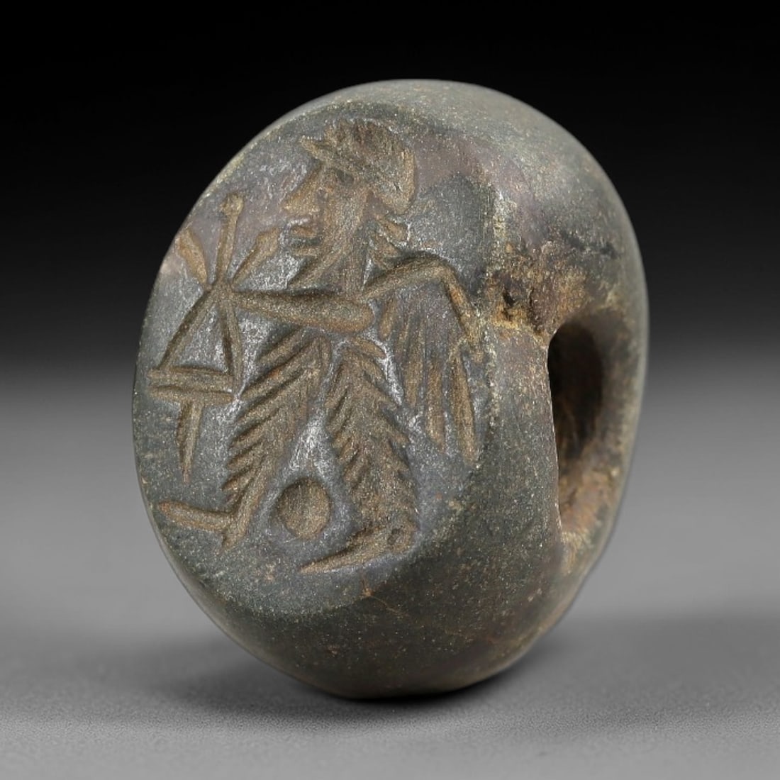 Ancient Stone Hemispherical Stamp Seal - Near Eastern Winged Deity Amulet, 28AN: This ancient Near Eastern hemispherical stamp seal is carved from a dense, dark stone, likely chlorite or steatite, with a weathered, earthy patina consistent with ancient burial contexts. The seal's