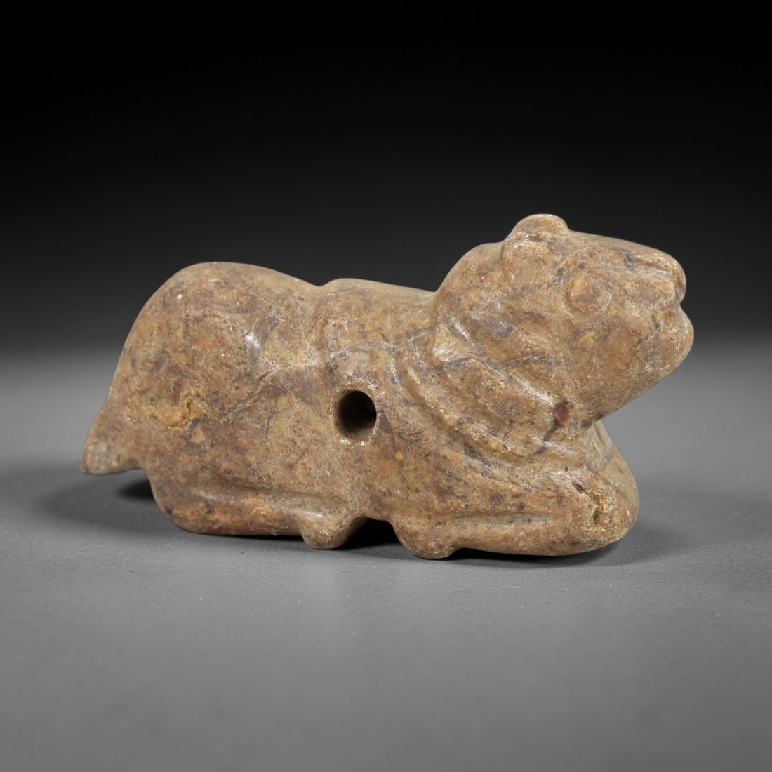 Ancient Stone Zoomorphic Amulet - Near Eastern Animal Figure, 55AM: This amulet is carved from speckled stone, depicting a stylized quadrupedal animal in a crouched, forward-leaning posture, with subtle incised lines defining the neck and facial features. The piece re