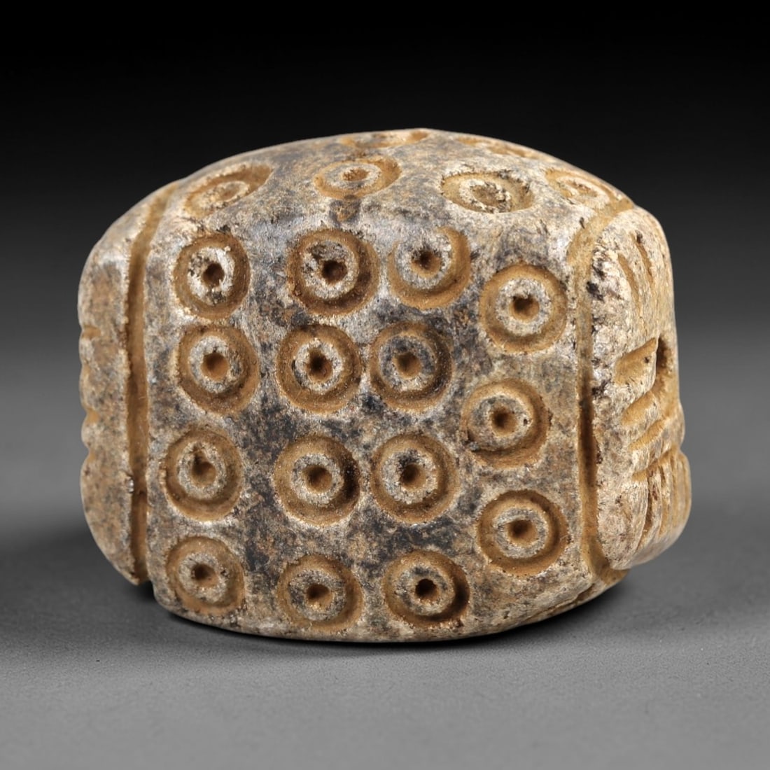Ancient Steatite Amulet - Near Eastern Concentric Circles, 40AK: Crafted from steatite, this rounded cubic amulet displays dense incised concentric circle motifs across its primary face, with vertical linear carvings along the lateral edges. A suspension hole pierc