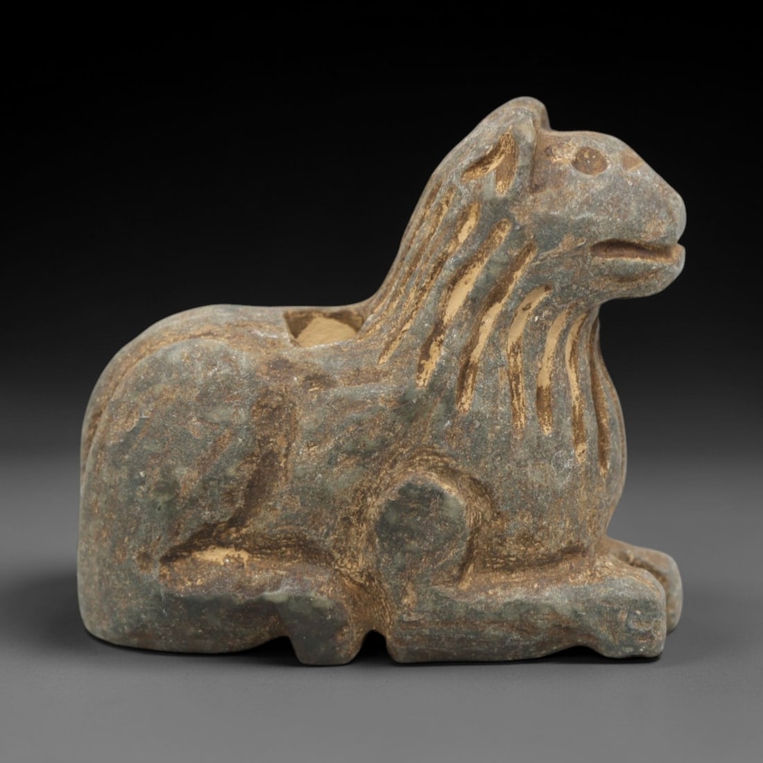 Ancient Stone Feline Amulet - Near Eastern Recumbent, 45ZR: Carved from muted green-grey stone with a naturally weathered, earthy patina, executed in a stylized recumbent form characteristic of Near Eastern zoomorphic amulet craftsmanship. The figure depicts a