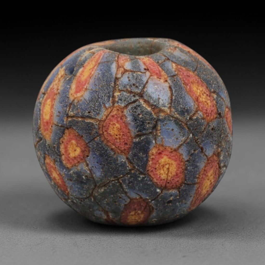 Ancient Glass Bead - Roman Egyptian Mosaic Amulet, 37ZN: Crafted from mosaic glass, this spherical bead features a central suspension hole and is decorated with repeating circular flame-like motifs in red, yellow, and blue glass inlay, characteristic of Rom