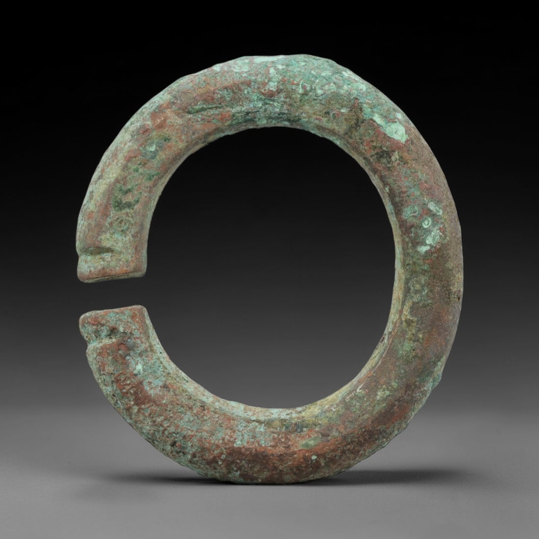 A Roman Bronze Bracelet, 1st-3rd Century CE, 93FT: Cast from bronze with a robust, fully rounded section, the bracelet is formed as an open C-shape with distinct, squared terminals featuring shallow incised notches at the edges. The surface exhibits a