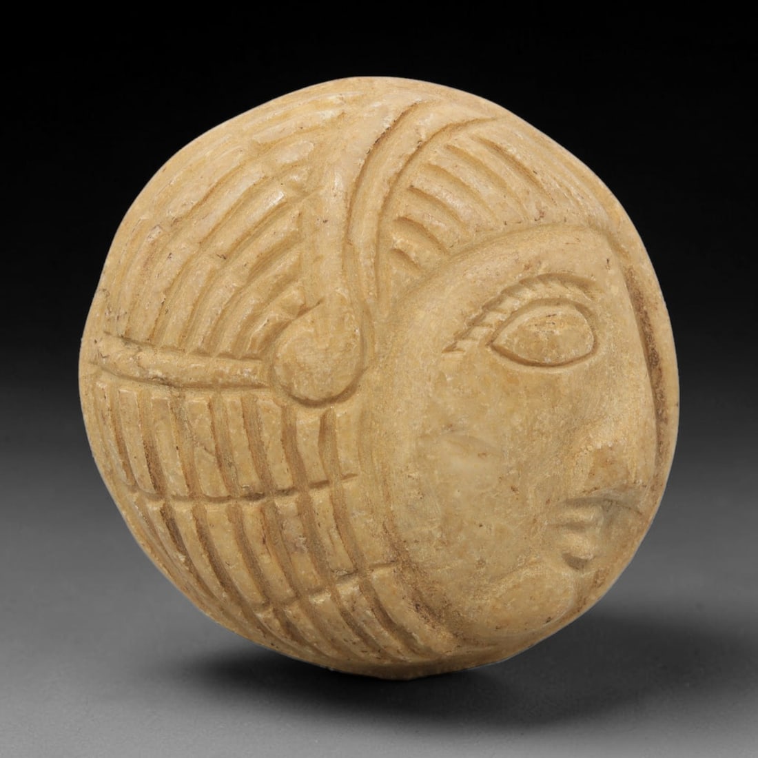 Ancient Stone Amulet - Near Eastern Bust Plaque Pendant, 30ZX: Carved from light-colored stone, the amulet is a spherical plaque crafted in the ancient Near Eastern style, featuring a raised relief portrait of a human bust in profile. The surface bears incised de
