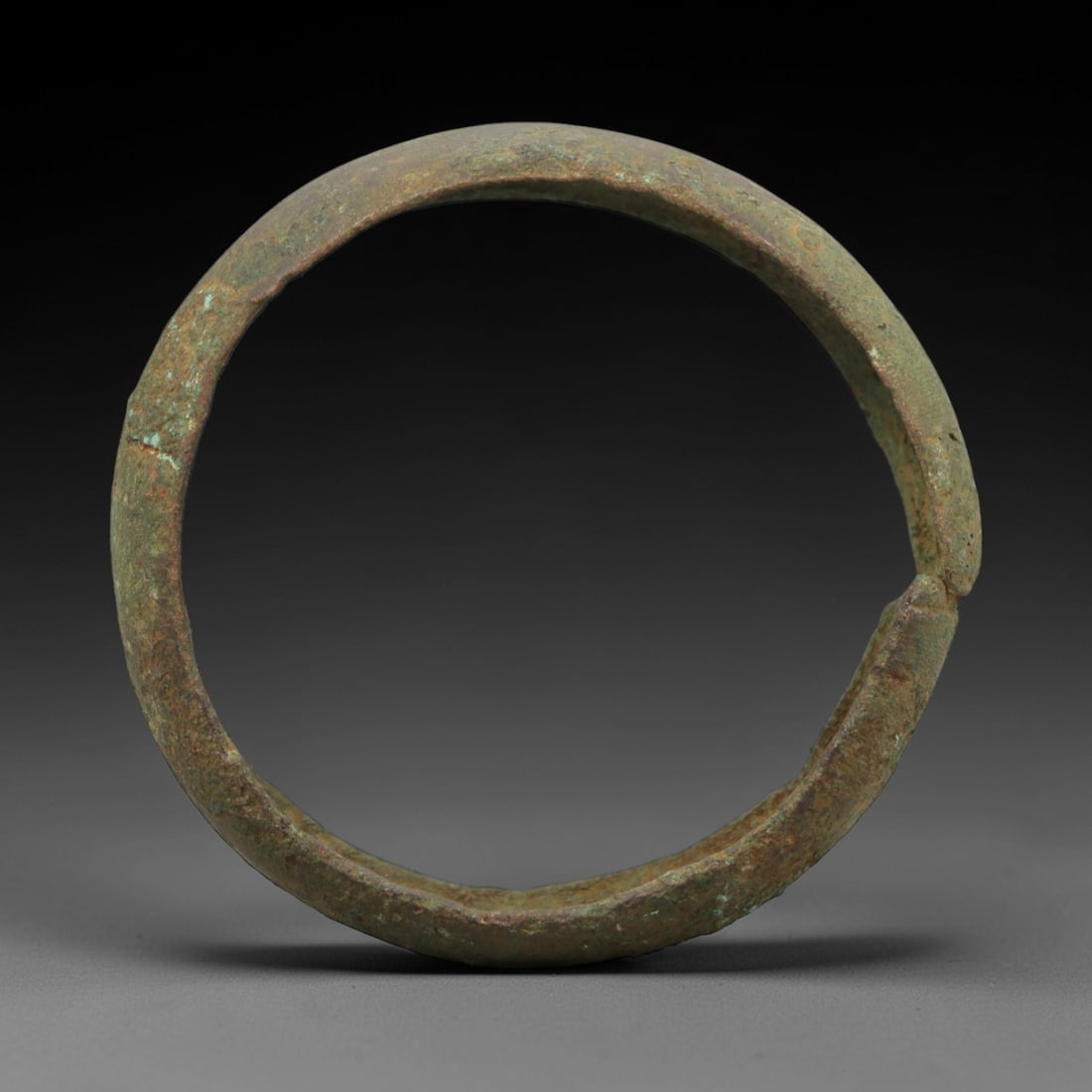 A Roman Bronze Bracelet, 1st-3rd Century CE, 7FV: Cast from bronze with a flattened, slightly curved section, the bracelet is formed as a near-complete circle with a narrow, overlapping terminal joint. The surface is covered in a patchy green and bro