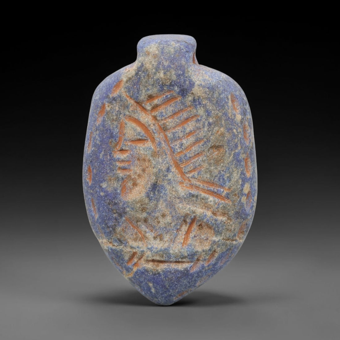 Ancient Lapis Lazuli Human Head Amulet - Near Eastern Carved Pendant, 25WJ: Carved from lapis lazuli, this pendant takes the form of a flattened, teardrop-shaped amulet, featuring an incised profile of a human head rendered in a stylized ancient Near Eastern artistic traditio