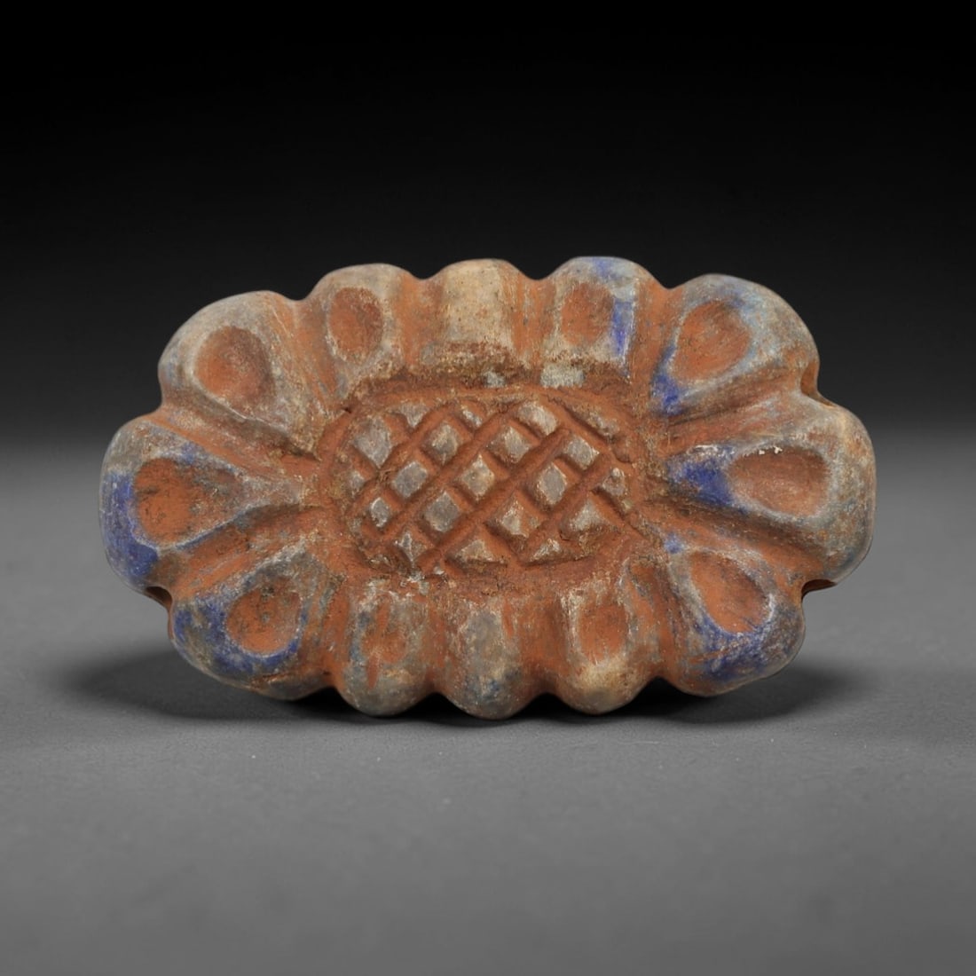 Ancient Lapis Lazuli Bead - Achaemenid Amulet, 45AH: Carved from lapis lazuli, this ancient Achaemenid bead features a scalloped form with an intricate geometric lattice pattern and a central perforation for suspension. The stone exhibits a deep, rich b