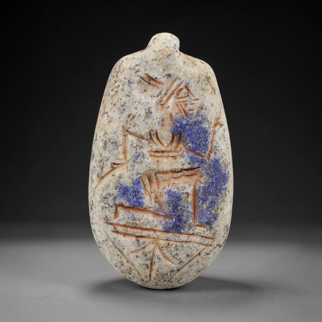Ancient Lapis Lazuli Amulet - Near Eastern Seated Figurine, 43BA: Carved from lapis lazuli, the amulet takes an oval, egg-shaped form with a suspension loop at the top, designed for wear as a protective talisman. The front face is incised with a seated anthropomorph