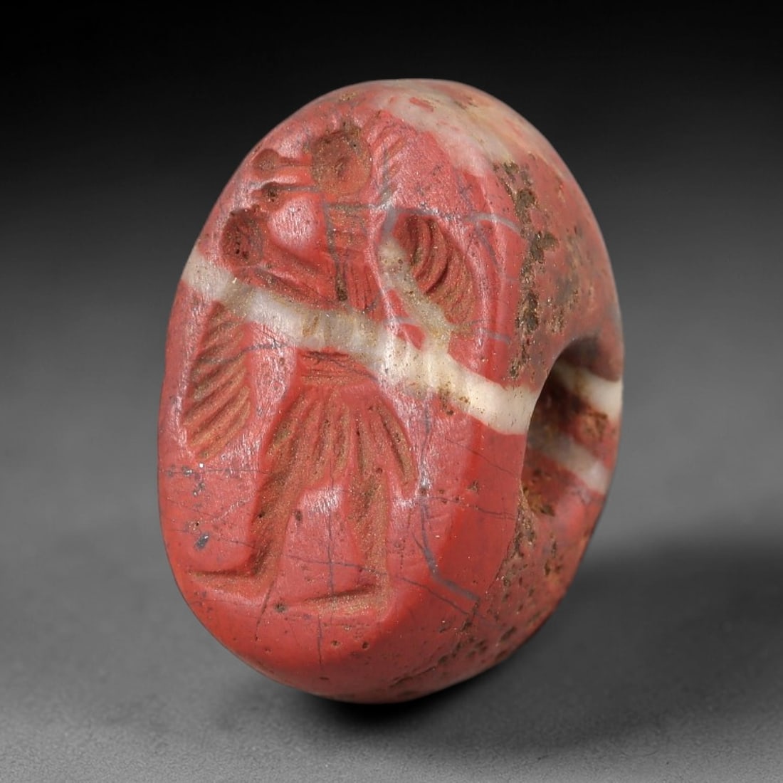 Ancient Jasper Stamp Seal - Near Eastern Bird-Headed Figure, 94AM: Carved from banded red-and-white jasper, this hemispherical stamp seal depicts a striding bird-headed anthropomorphic figure with outstretched wings and linear incised details defining its form and at