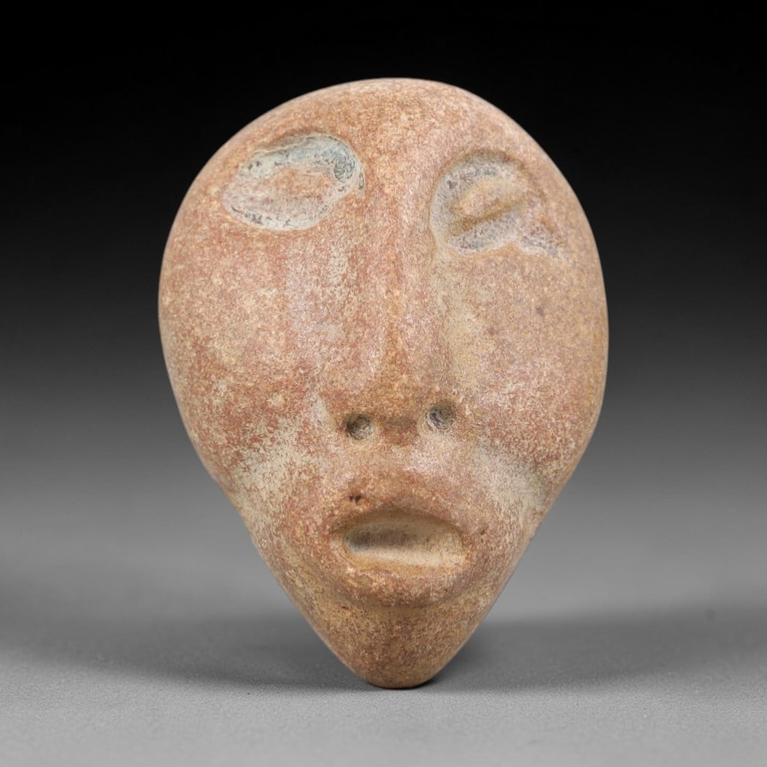 Ancient Stone Maskette - Medieval Figurine, 17FY: Carved from a smooth, teardrop-shaped stone, this maskette features a stylized human face with incised details defining the closed eyes, nasal perforations, and open mouth. Stylistically consistent wi
