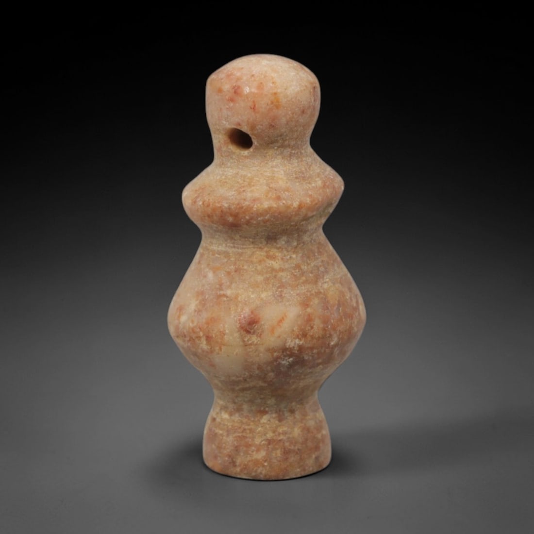 Ancient Stone Votive Amulet - Near Eastern Pendant, 28XQ: Carved from a speckled pinkish stone, this amulet takes a stylized, gourd-like form with a perforated top for suspension, indicative of wearable ritual use. The symmetrical, bulbous form is characteri