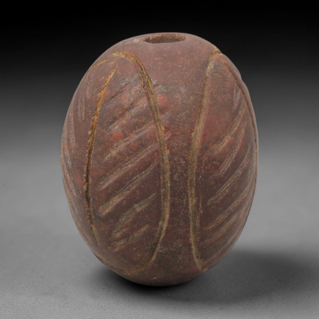 Ancient Egyptian Palm Leaf Amulet - Egyptian Stone Pendant, 32XQ: This amulet is carved from a rich, reddish-brown stone, shaped into an oval palm leaf form with a perforated suspension hole at one end, confirming its use as a wearable protective charm. The surface