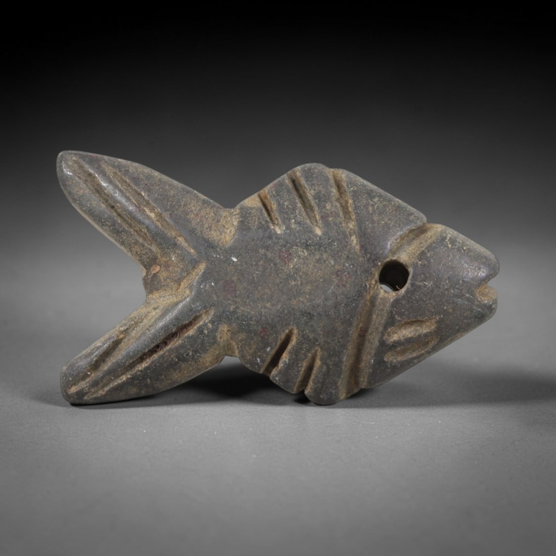 Ancient Stone Fish Amulet - Egyptian Ritual Pendant, 23AR: Carved from dark, weathered stone, this fish amulet follows a stylized avian-fish form with incised linear details defining the fins, tail, and facial structure, with a pierced hole near the head for