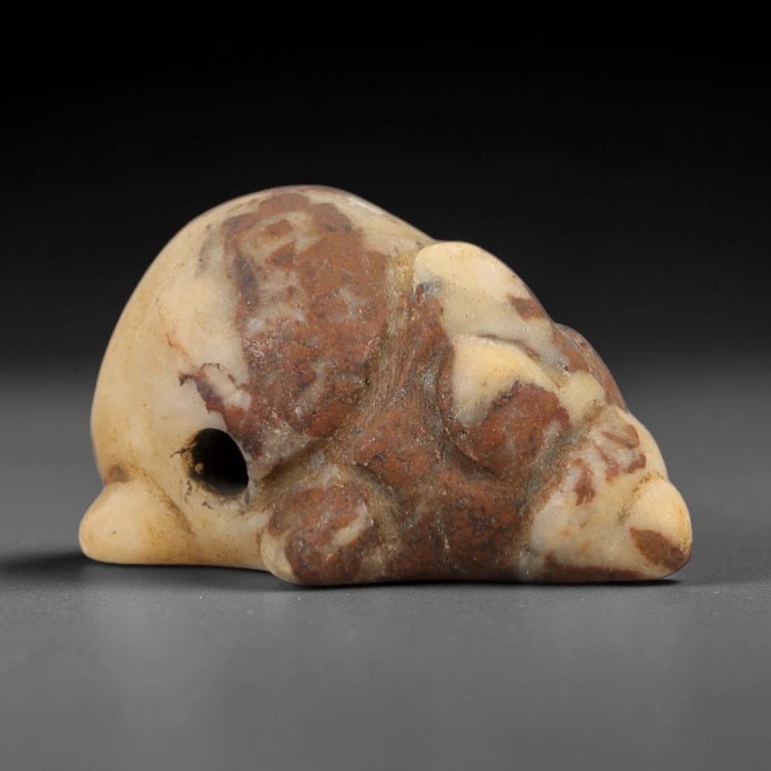 Ancient Mottled Stone Mouse Amulet - Near Eastern Relic, 85AD: Carved from cream and reddish-brown mottled stone, this amulet depicts a stylized mouse in a compact, recumbent form. The creature features simplified facial contours and a rounded body, with a drille