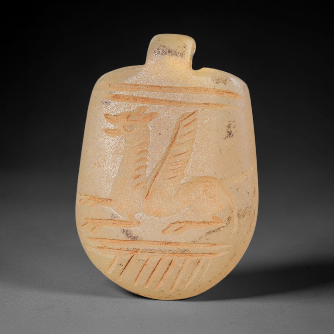 Ancient Stone Griffin Amulet - Near Eastern Carved Pendant, 14BA: Carved from translucent light-colored hardstone, the amulet takes the form of a flattened oval pendant with a drilled suspension lug at the top for wear. The surface features a relief-carved stylized